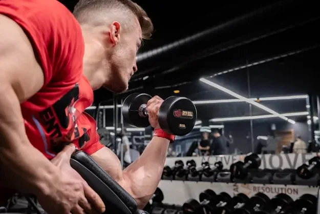 Man in a red vest performing a dumbbell biceps curl in the gym