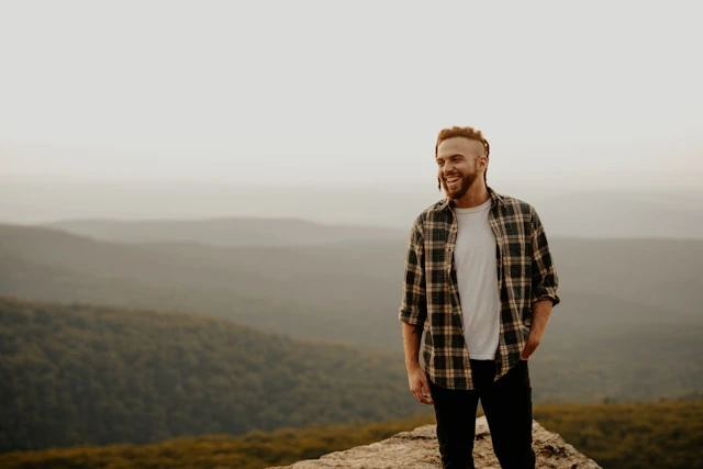 Smiling man standing on a rocky ridge with wooded mountain ranges behind him