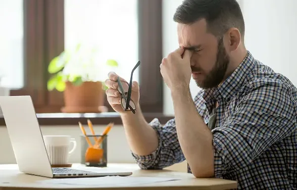 Tired man at his laptop holding his glasses in one hand